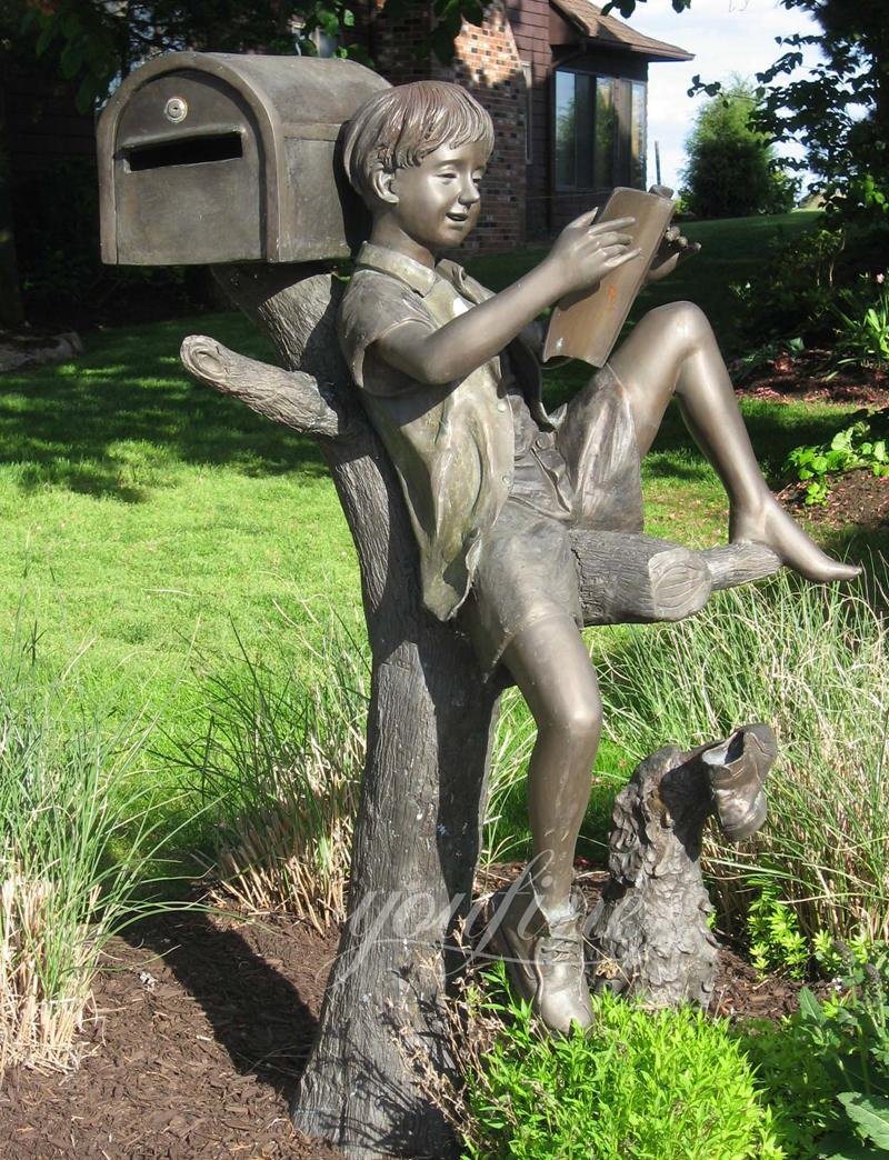 life size bronze sculpture of a little boy sitting in a tree reading a book